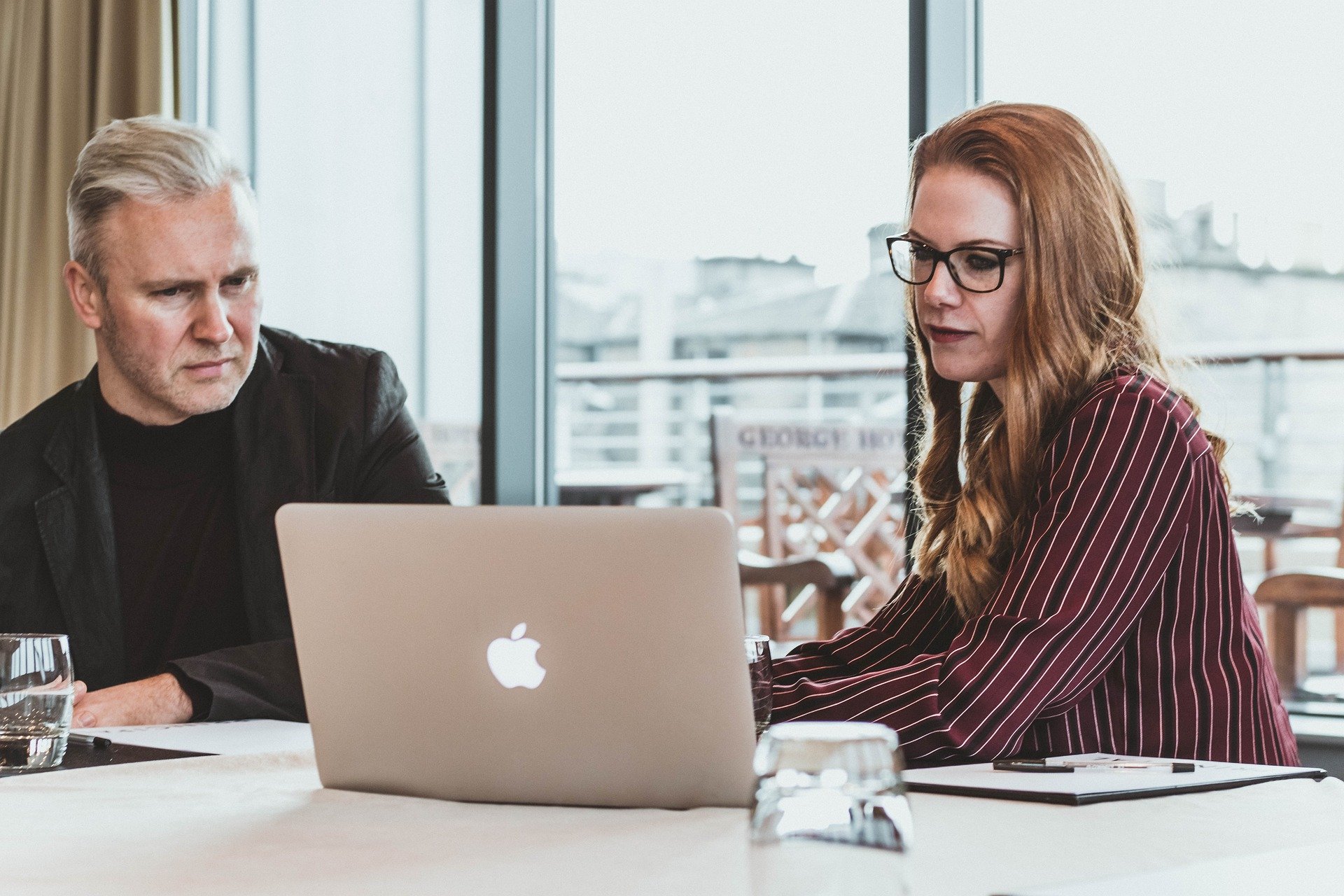 man-and-woman-sitting-at-table-and-watching-virtual-event-on-laptop