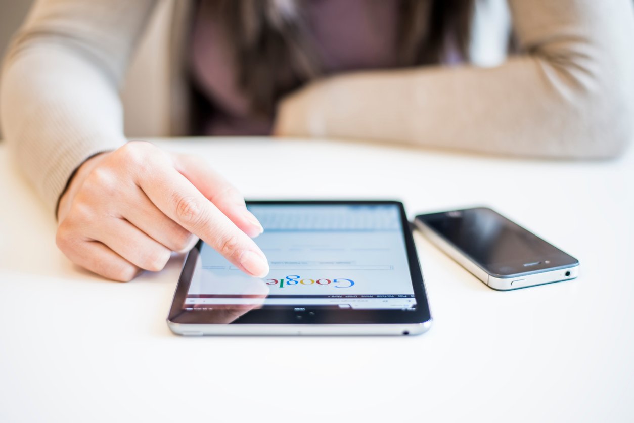 woman-using-tablet-to-search-google-at-table-with-smartphone-nearby