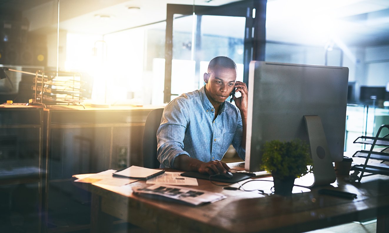 man sitting at desk using computer and cell phone