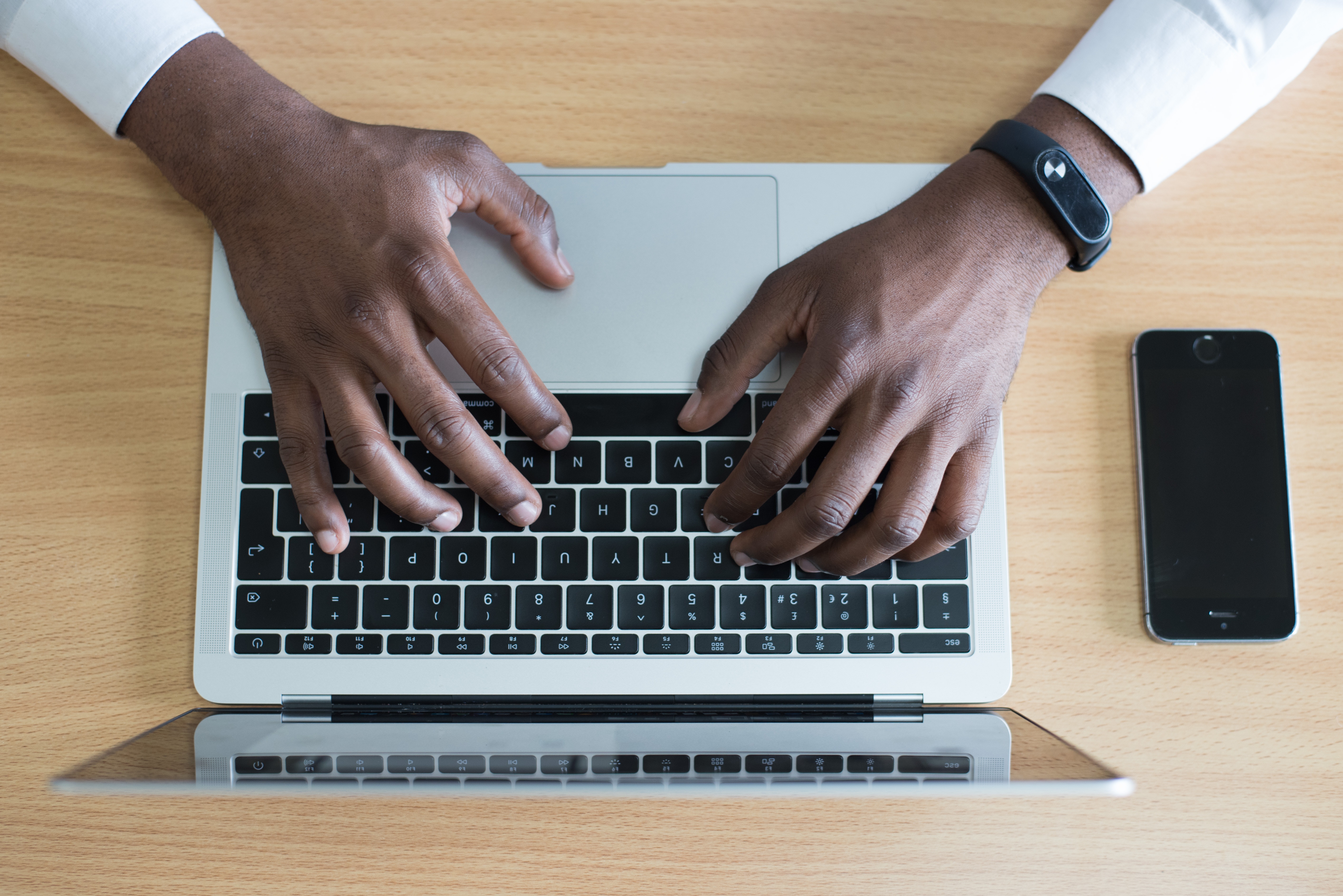 bird's-eye-view-of-hands-typing-on-laptop-with-smartphone-on-table-next-to-laptop