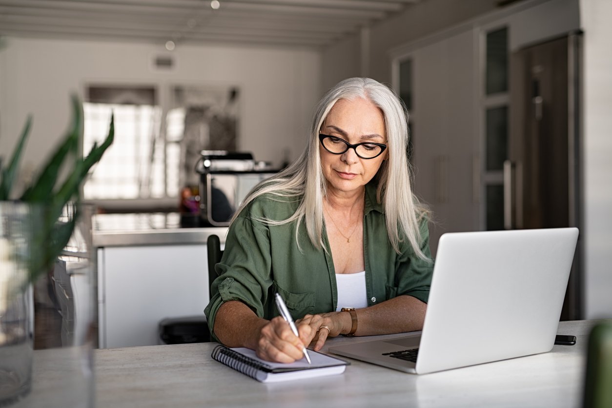 journalist-working-from-home-with-laptop-and-writing-in-pad-of-paper